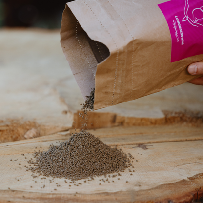 braunes Cystus Equine Granulat, das aus einer braunen Verpackung mit pinkem Etikett geschüttet wird und einen Haufen auf einer Holzplatte bildet