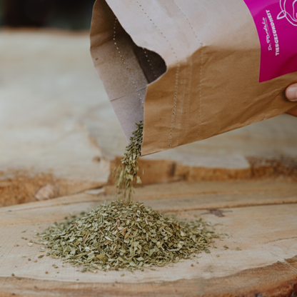 hellgrünes Cystus Equine Zistrosenkraut, das aus einer braunen Verpackung mit pinkem Etikett geschüttet wird und einen Haufen auf einer Holzplatte bildet